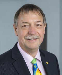 Headshot of Dr. Steve Carstensen wearing black suit jacket, purple shirt and multi colored tie